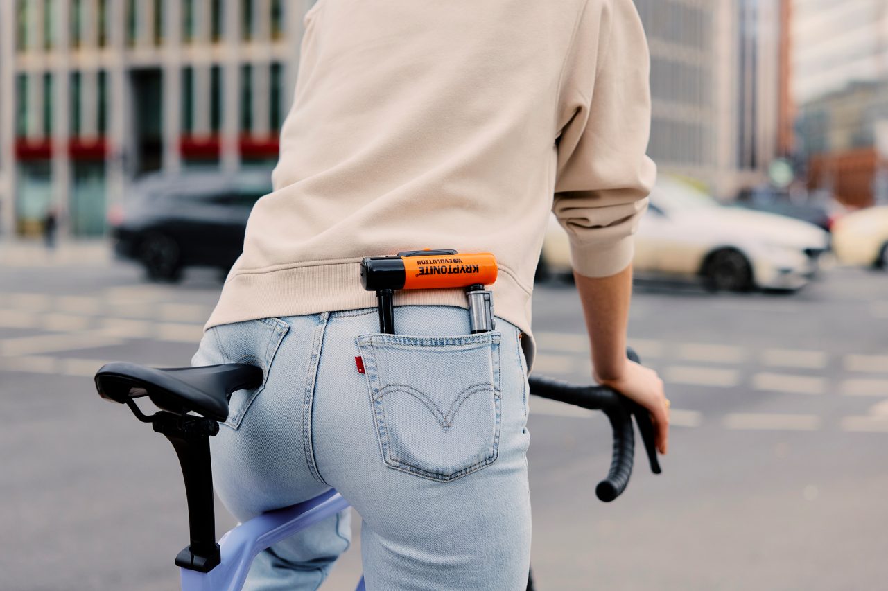 A person in a yellow shirt standing with a bicycle, with a red light illuminated under the bike seat, in an urban setting.