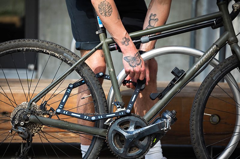 A person holding a yellow Kryptonite lock next to a pink bicycle, wearing a black shirt and a coiled keychain on their wrist.